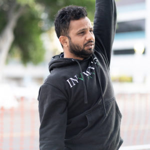 Male athlete doing a weighted overhead carry outside of the gym.