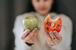 Woman holding a Granny Smith apple in one hand and a sprinkle donut with a bite out of it in the other.