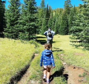 A father and daughter hiking into the woods.