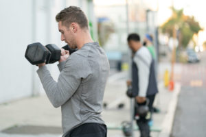 Line of athletes outside of the gym doing biceps curls the sunshine.