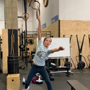 Female teen athlete hanging from a gymnastics ring with one arm.