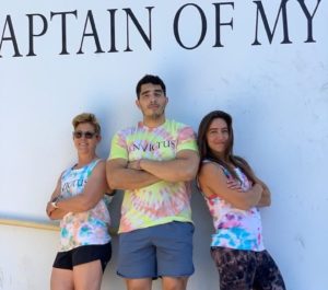 Three athletes with arms crossed and wearing tie-die lean against a wall with an inspirational quote.