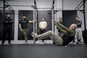 Invictus Gymnastics coach laying on his back with a PVC pipe demonstrating a bar muscle-up drill at a seminar.