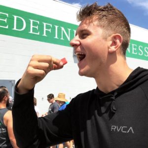 A male athlete eating a slice of watermelon at a potluck outside of the gym.